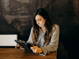 Women Wearing Grey Sweater Sitting at Desk While Looking Down at Black Laptop